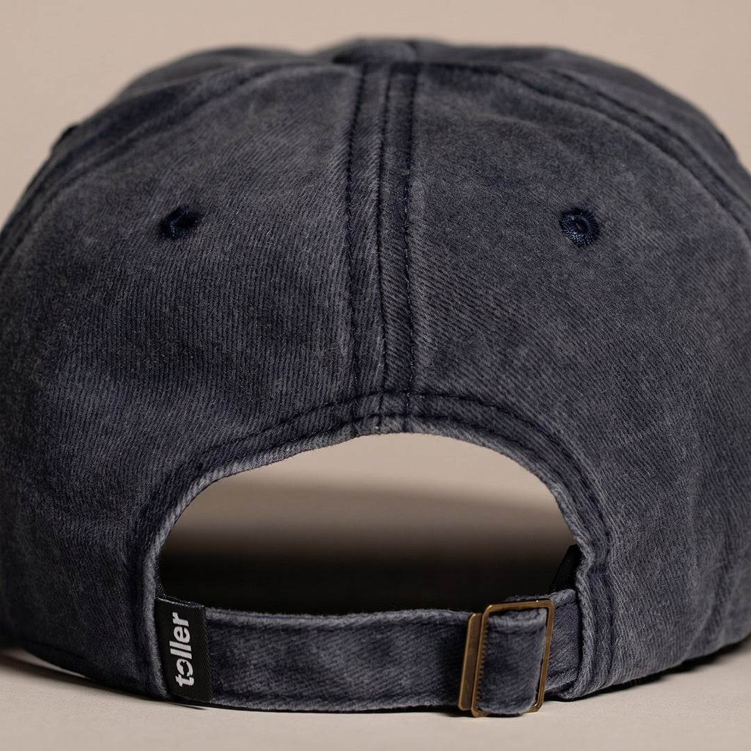 Back view of a dark gray cap with a brown strap on a beige background