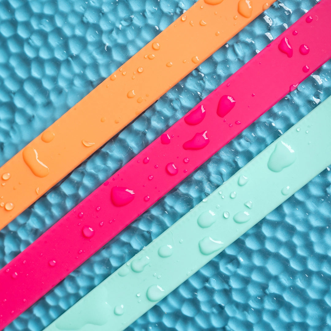 Three colorful rubber bands (orange, pink, green) on a textured blue surface with water droplets.