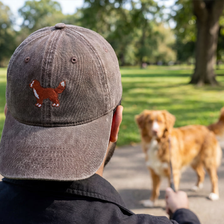 Person wearing a cap with a dog logo in a park with dogs.