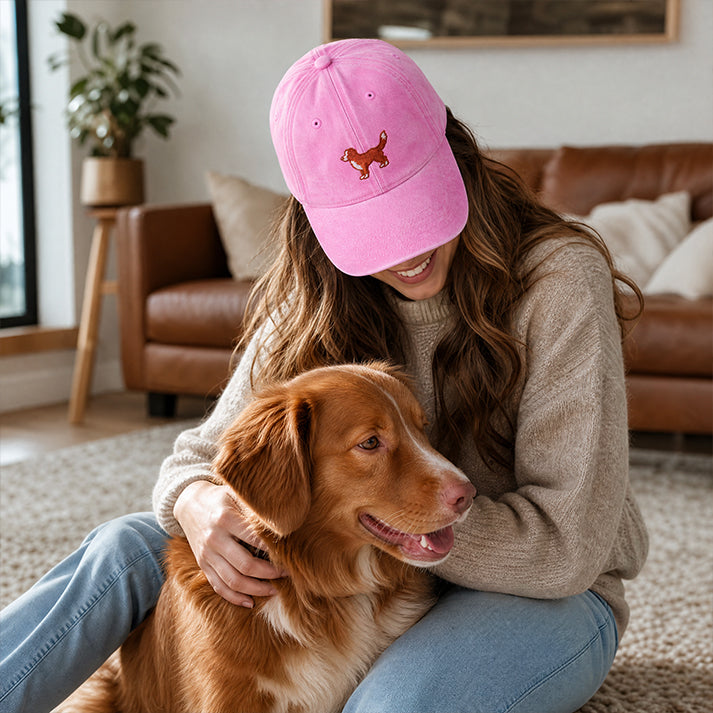 Woman wearing a pink cap with a dog logo, sitting on the floor with a brown dog in a living room.