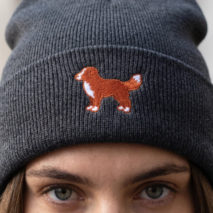 Gray knit beanie with embroidered dog design worn by a person.