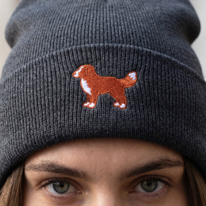 Gray knit beanie with embroidered dog design worn by a person.