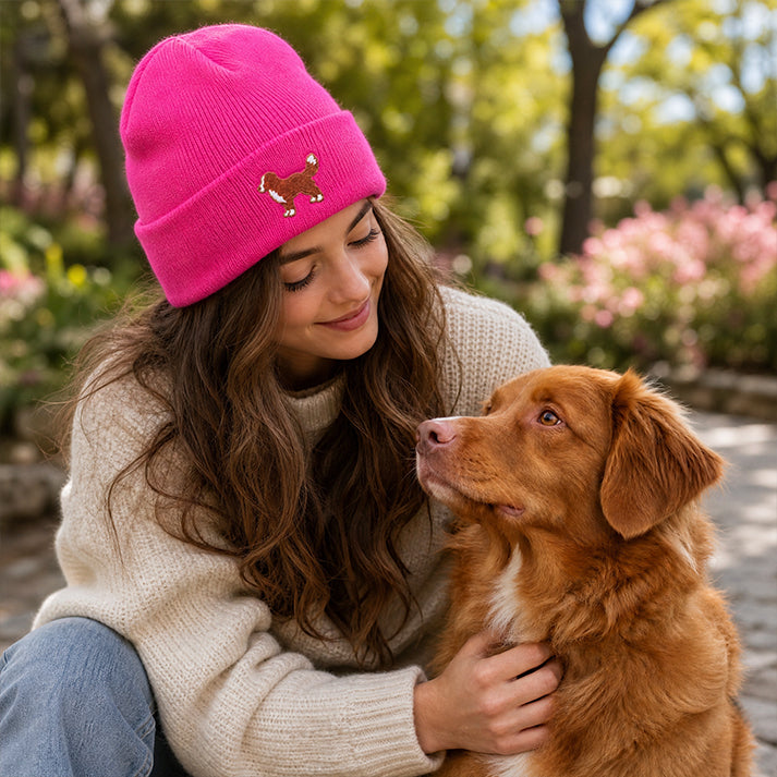 Woman wearing a pink beanie with a dog logo, sitting outdoors with a brown dog.