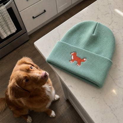 Green beanie with a dog design on a kitchen counter next to a brown dog.