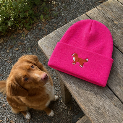Pink beanie with dog design on a wooden bench next to a brown dog outdoors.