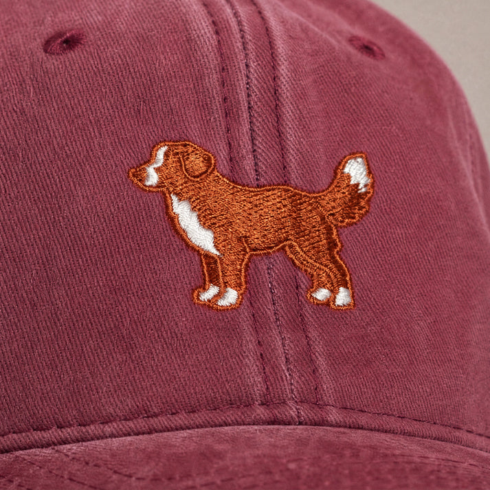 Maroon cap with embroidered dog design on a beige background