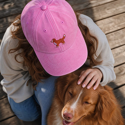 Person wearing a pink cap with a dog design, petting a brown dog on a wooden deck.