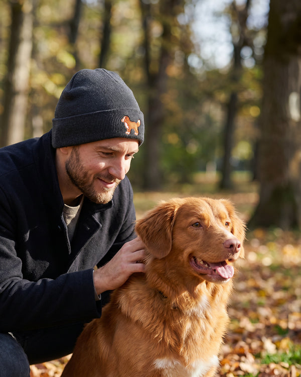Man petting a brown dog in a park with trees and fallen leaves in the background