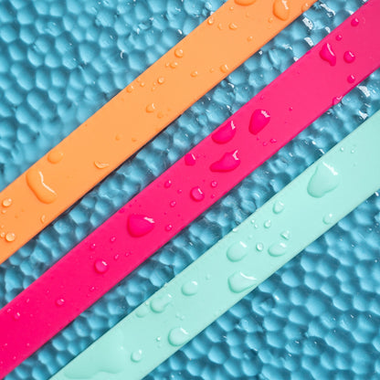 Three colorful rubber bands (orange, pink, green) on a textured blue surface with water droplets.